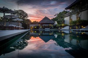 - une piscine avec un kiosque et un coucher de soleil dans l'établissement REVĪVŌ Wellness Resort Nusa Dua Bali, à Nusa Dua
