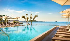
a beach with a pool, chairs, and umbrellas at Resort Amarin in Rovinj

