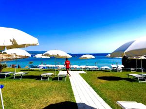 a person walking down a path with chairs and umbrellas at Hotel Punta Negra in Alghero