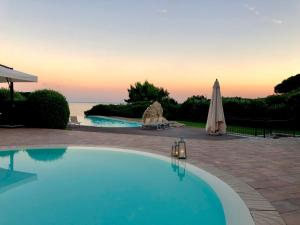 a large swimming pool with an umbrella and the ocean at Hotel Punta Negra in Alghero