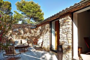 a patio with chairs and a table and a stone wall at Hôtel - le Jas de Joucas in Joucas