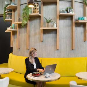 a woman sitting on a yellow couch with a laptop at Novotel Paris Charles de Gaulle Airport in Roissy-en-France