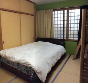 a bedroom with a bed with white sheets and two windows at Kamikatsura House in Kyoto