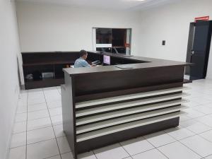 Ein Mann sitzt an einem Tresen in einem Büro in der Unterkunft Hotel Águia in Teixeira de Freitas