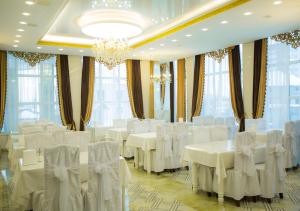 um salão de banquetes com mesas e cadeiras brancas e janelas em Hotel Alash em Astana