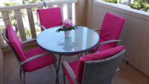 une table en verre avec des chaises roses et une fleur sur un balcon dans l'établissement Apartment Adrijana, à Novalja