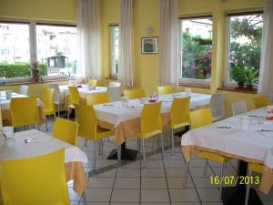a restaurant with white tables and yellow chairs and windows at Hotel Toresela Bike am Gardasee in Nago-Torbole