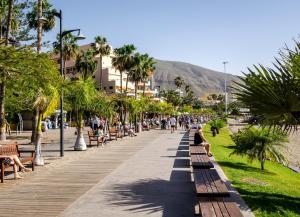 a boardwalk with people sitting on benches and palm trees at Royal Stylish sea view in Los Cristianos