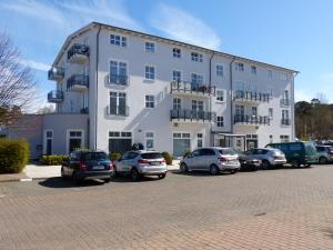 ein großes weißes Gebäude mit auf einem Parkplatz geparkten Autos in der Unterkunft Ferienwohnung 14 - Sofia Haus Hühnergott in Ostseebad Sellin