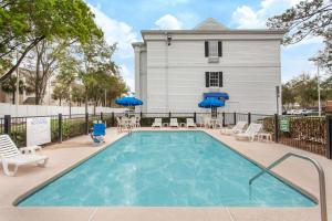 einen Pool mit Stühlen und Sonnenschirmen vor einem Haus in der Unterkunft Baymont by Wyndham Jacksonville/Butler Blvd in Jacksonville
