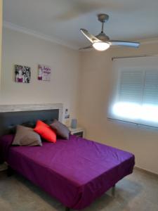 een slaapkamer met een paars bed en een plafondventilator bij Bonito apartamento in Torre del Mar