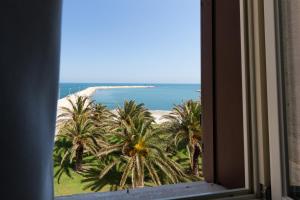 a window view of a beach with palm trees and the ocean at Palazzo Filisio - Regia Restaurant in Trani