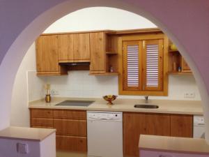 una cucina ad arco con armadi in legno e lavastoviglie bianca di Casa Victor a Playa Migjorn