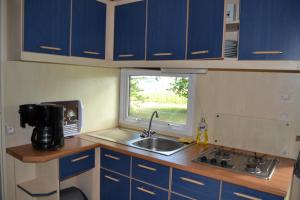 a kitchen with blue cabinets and a sink and a window at Mobile home des pins in Châtignac