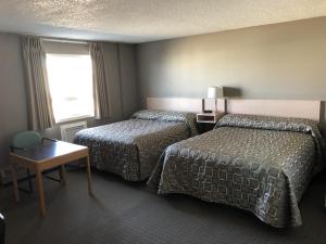 KindersleyにあるArbour Ridge Inn & Suitesのベッド2台、テーブル、窓が備わるホテルルームです。