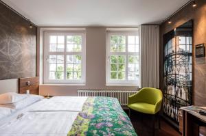 a bedroom with a bed and a green chair at Mintrops Stadt Hotel Margarethenhöhe in Essen