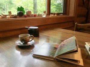 a book on a wooden table with a cup and a coffee mug at Canadian Loghouse Inn AzuminoYujin in Azumino