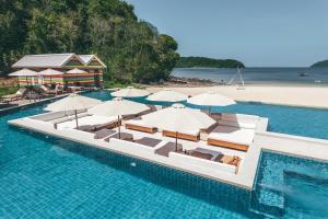 an infinity pool with chairs and umbrellas and a beach at Dash Resort Langkawi in Pantai Cenang