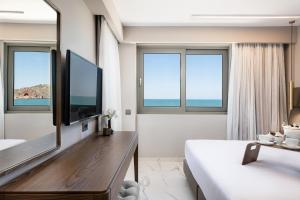 a bedroom with a bed and a tv and windows at Porto Platanias Beach Luxury Selection - Adults Only in Plataniás