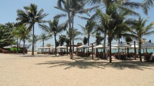 a beach with palm trees and tables and umbrellas at Casa CANTIN DO ACONCHEGO na Praia de Taperapuan, Porto Seguro in Porto Seguro