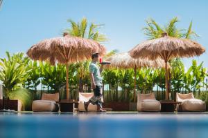 un hombre caminando bajo dos grandes sombrillas de paja en Mahogany Hotel, en Nusa Dua