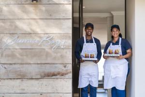 a man and woman in aprons holding boxes of food at Sunrise Bay Self Catering in Plettenberg Bay