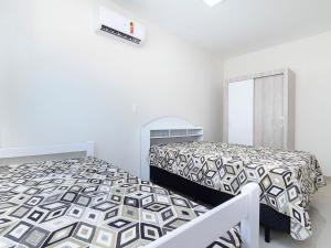 Habitación blanca con 2 camas y espejo. en Aluguel Apartamento 2 quartos sendo 1 suíte Bombas/SC, en Bombinhas