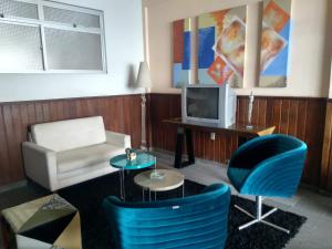 a living room with blue chairs and a tv at Sollarium GINI Suítes in Guarapari