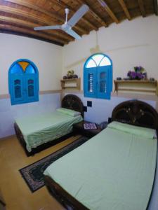 een kamer met 2 bedden en 2 blauwe ramen bij villa tunis village in ‘Izbat an Nāmūs