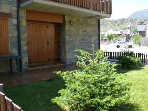 un árbol frente a una casa con una puerta de madera en Apartamentos wifi Baqueira & Aigüestortes con jardín privado, en Esterri d'Àneu