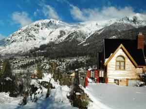 una casa en la nieve frente a una montaña en Cabañas Aquelarre Catedral en San Carlos de Bariloche