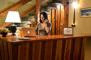 een vrouw die aan een bureau met een laptop met een mobiele telefoon praat bij Hostería Güemes in Bariloche