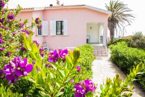 una casa rosa con fiori viola di fronte di Villa Diana affitta camere a Stintino