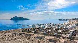 a beach with chairs and umbrellas and the ocean at Porto Platanias Beach Luxury Selection - Adults Only in Plataniás