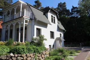 a white house with a porch and a stone wall at Villa Waldheim - WG 2 in Boltenhagen