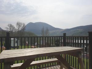 a wooden bench on a deck with mountains in the background at Lletyr Bugail in Caernarfon