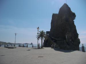 a rock formation next to the beach with people and the ocean at Oasis in Acitrezza