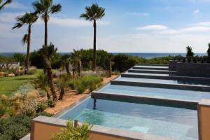 a swimming pool with palm trees and the ocean at Hipotels Playa La Barrosa - Adults Only in Chiclana de la Frontera