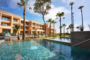 a swimming pool in front of a building with palm trees at Hipotels Playa La Barrosa - Adults Only in Chiclana de la Frontera