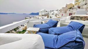 uma varanda com cadeiras azuis e vista para a água em Aqua & Terra Traditional Cave Houses em Oia