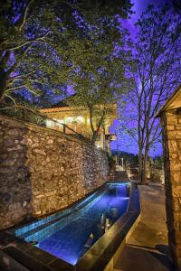 a swimming pool next to a stone wall at night at Santa Marina Guesthouse in Kato Loutraki