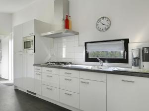 a white kitchen with a sink and a clock on the wall at Chic Forest Lodge with Sauna in Markelo