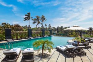 a pool at a resort with lounge chairs and an umbrella at The Acacia Morjim in Morjim