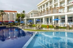 a hotel swimming pool with chairs and blue umbrellas at Marupiara Resort in Porto De Galinhas