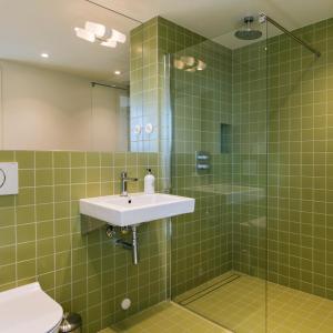 uma casa de banho com azulejos verdes, um lavatório e um chuveiro em Trevarefabrikken em Henningsvær