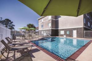 - une piscine avec des chaises longues et des chaises à côté d'un bâtiment dans l'établissement La Quinta by Wyndham Walker - Denham Springs, à Walker