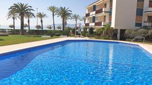 a swimming pool in front of a building with palm trees at Playazul seafront apartament in Cambrils