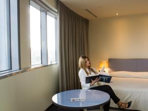 a woman sitting in a hotel room reading a book at UNAHOTELS T Hotel Cagliari in Cagliari