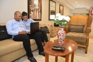 two people sitting on a couch with a laptop at Emakhosini Self-Catering Apartments in Durban