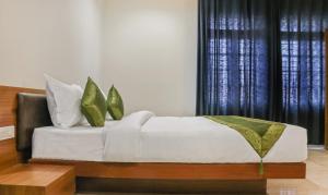 a bed with white sheets and green pillows in a room at Treebo Trend Casino in Kozhikode